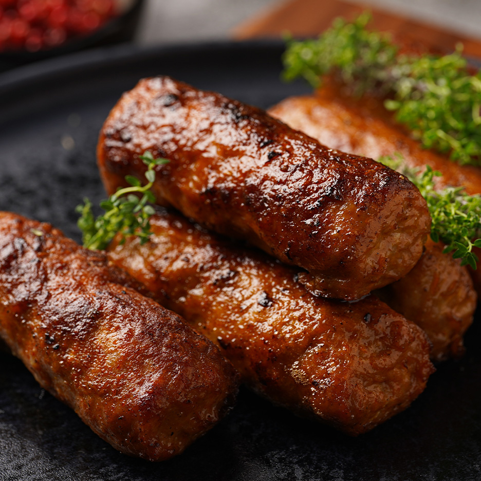 Nærbillede af gyldenbrune, grillede pølser pyntet med friske krydderurter på en mørk tallerken.