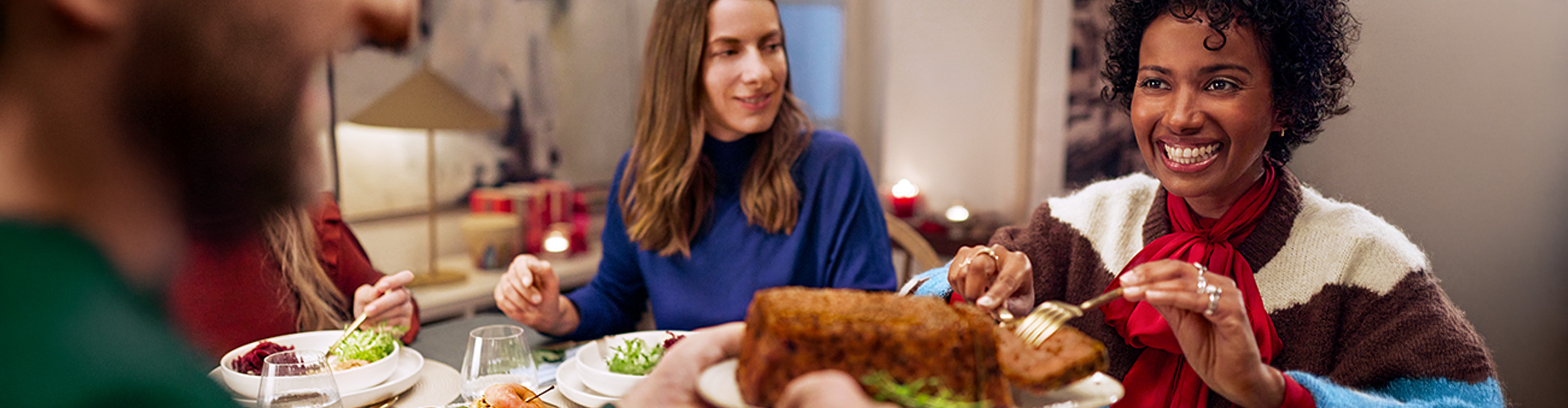 Glade venner deler et festmåltid med brød og salater ved et bord.