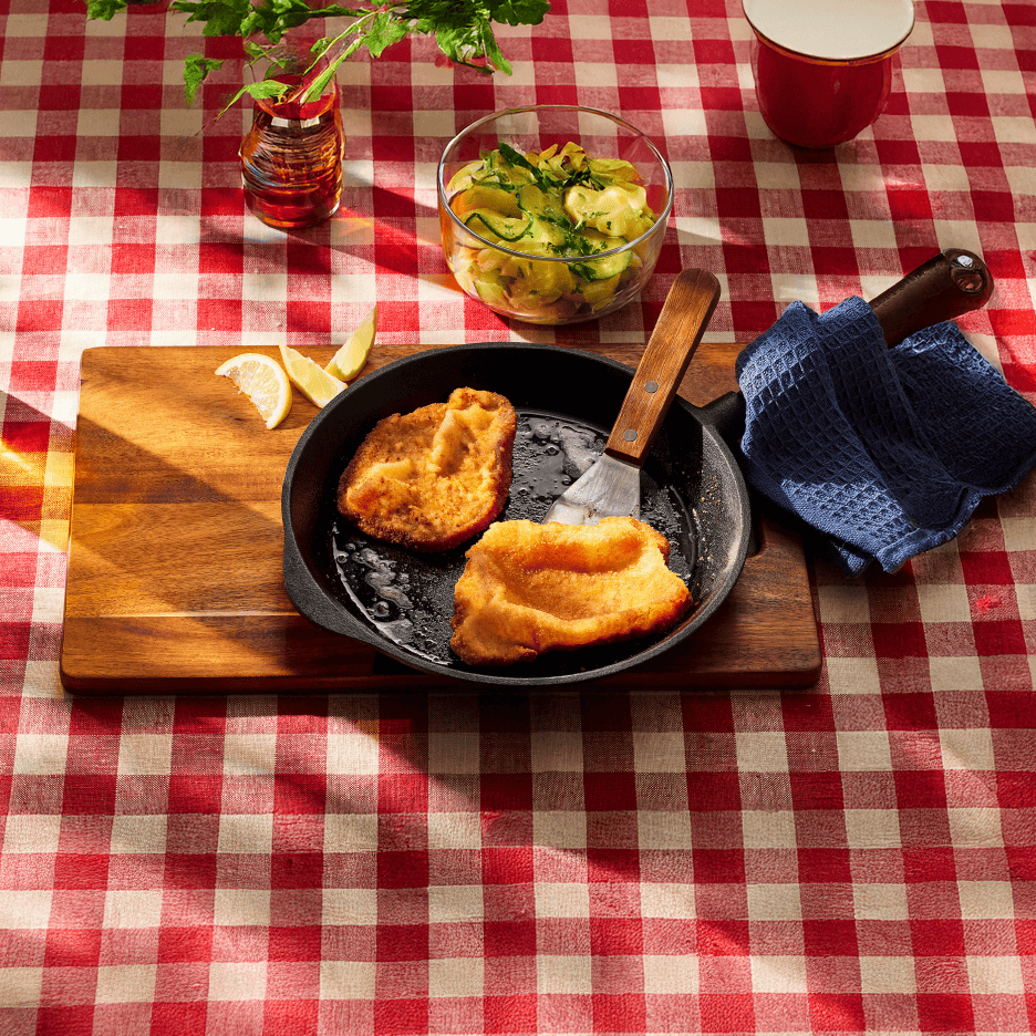 Stegt schnitzel i pande med citron, agurkesalat og rødternet dug.