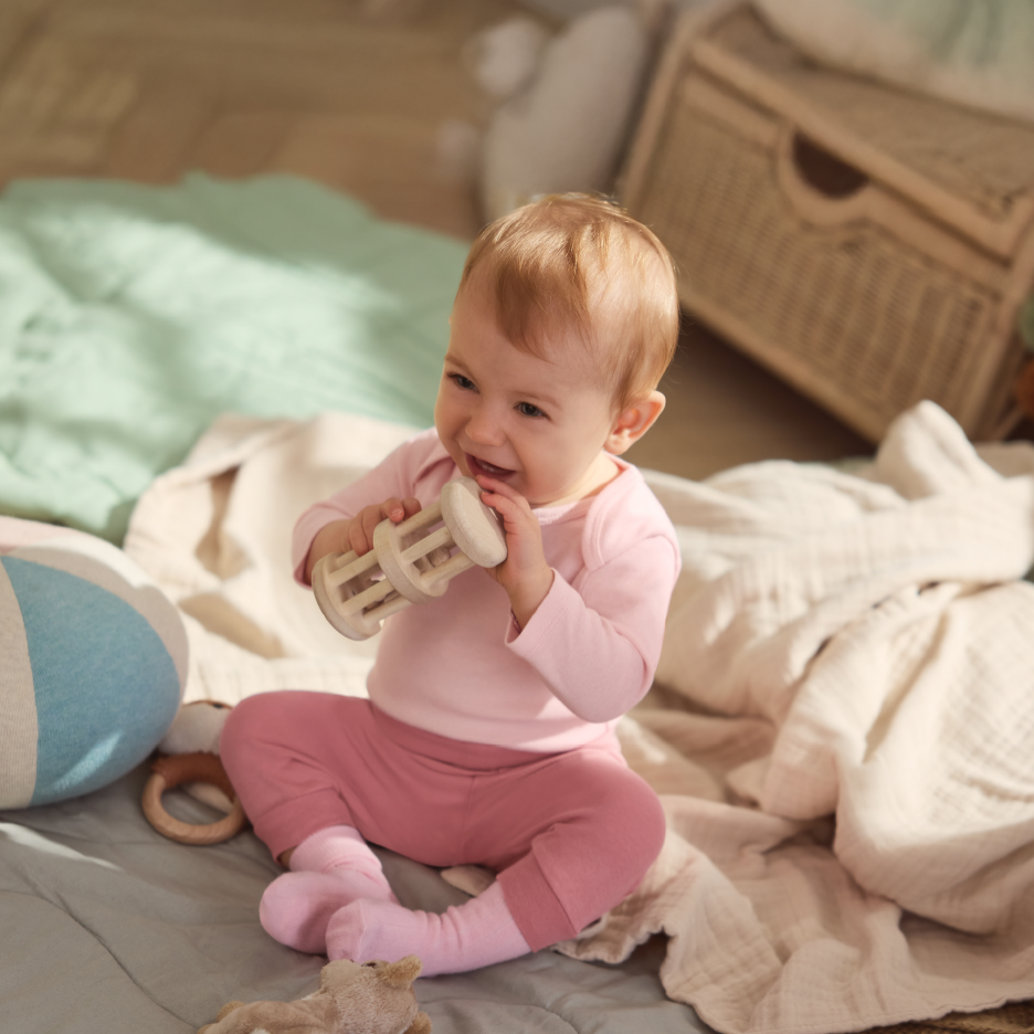 Glad baby i lyserødt tøj leger med trærangle på et tæppe.