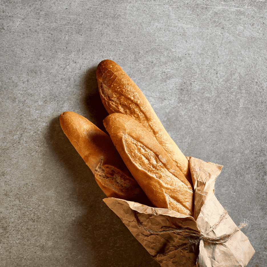 Tre sprøde baguettes i brunt papir på en grå baggrund.