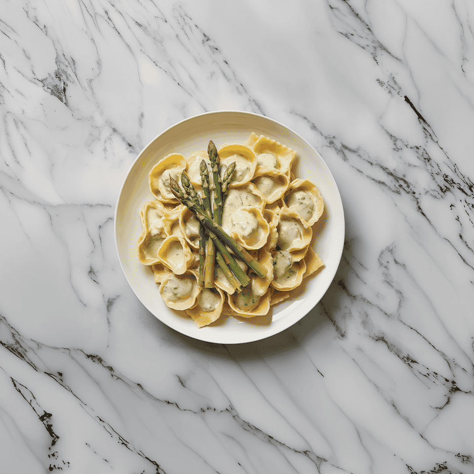 Ravioli med cremet sauce og asparges på en hvid marmorplade.