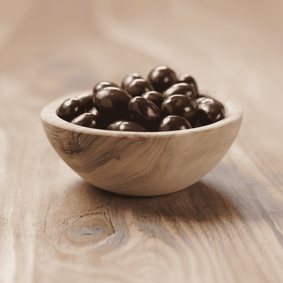 En træskål fyldt med mørke chokoladeovertrukne nødder på et træbord.
