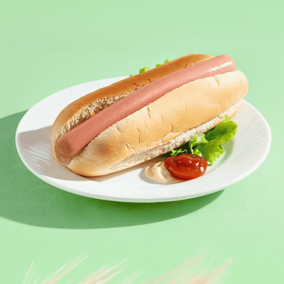 En hotdog med salat, ketchup og mayonnaise på en hvid tallerken.