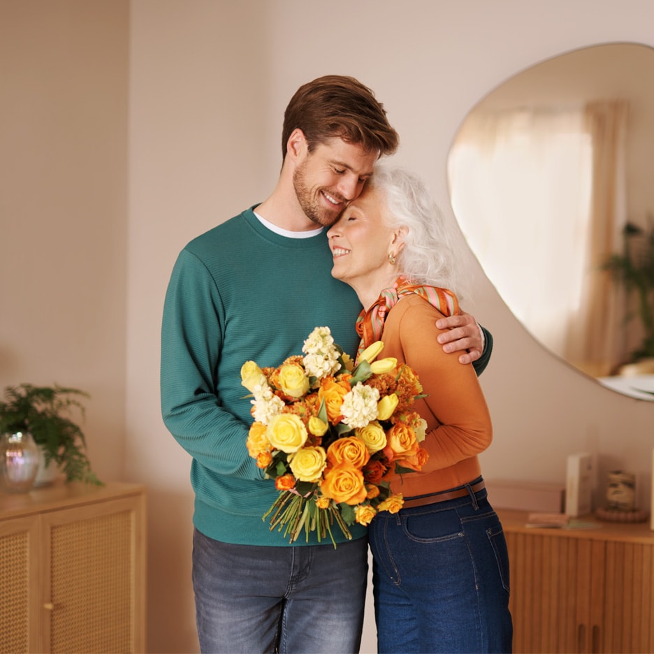 Mand og kvinde krammer, kvinden holder en buket gule og orange blomster.
