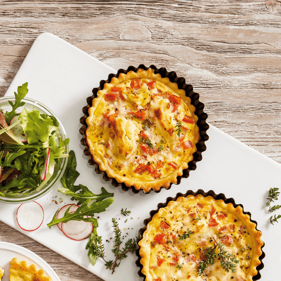 To små quicher med salat og radiser på et hvidt fad.