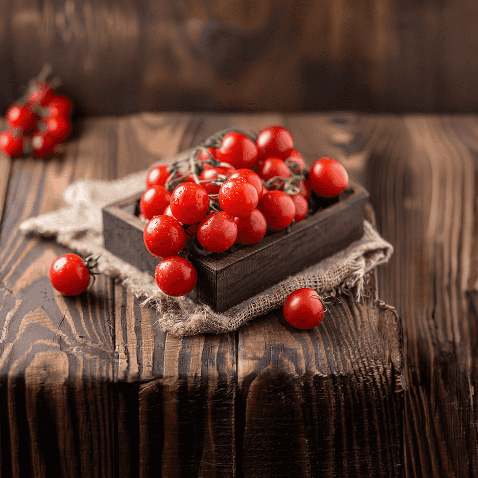 Friske cherrytomater på stilk i en trækasse på et rustikt træbord.