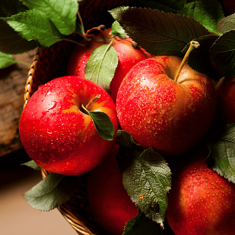 Friske røde æbler med grønne blade i en kurv, dækket af vanddråber.