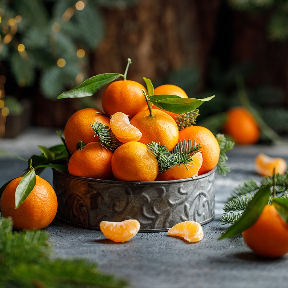 Friske mandariner med grønne blade og grangrene i en rustik skål.