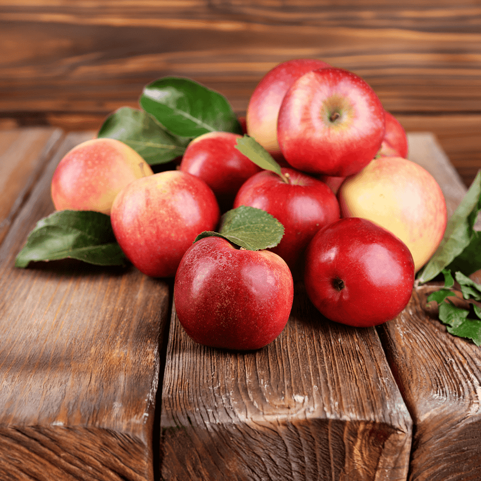 En bunke røde og gule æbler med grønne blade på et træbord.