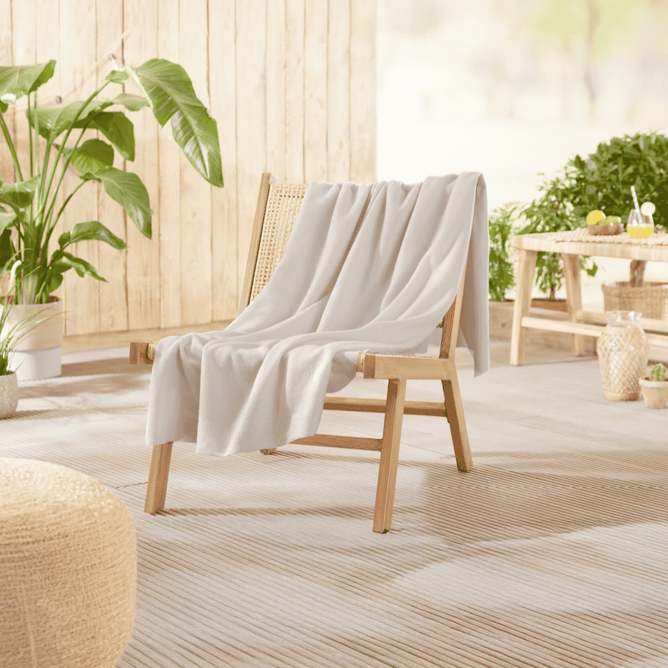 Beige tæppe draperet over en træstol på en terrasse med planter og et bord.
