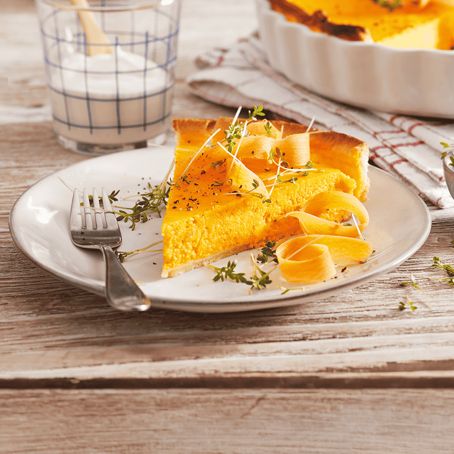 Et stykke græskartærte med gulerodsstrimler og krydderurter på en tallerken.