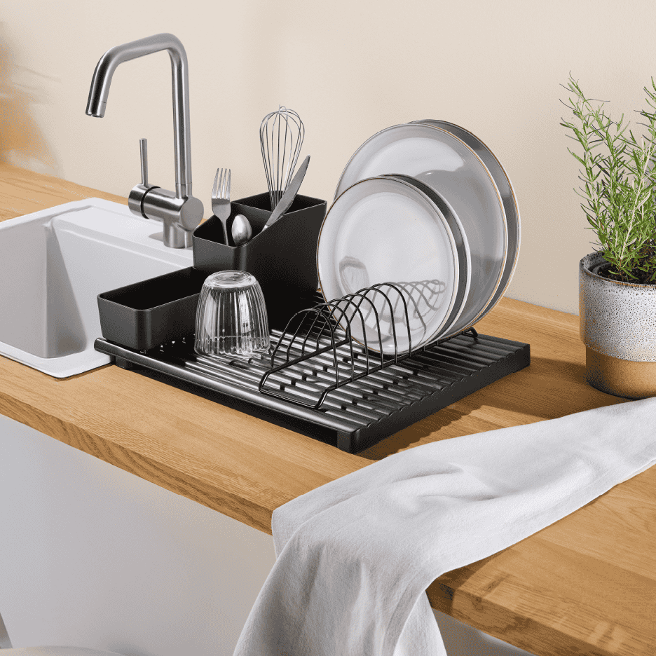 Sort opvaskestativ med tallerkener, bestik og glas ved en køkkenvask.