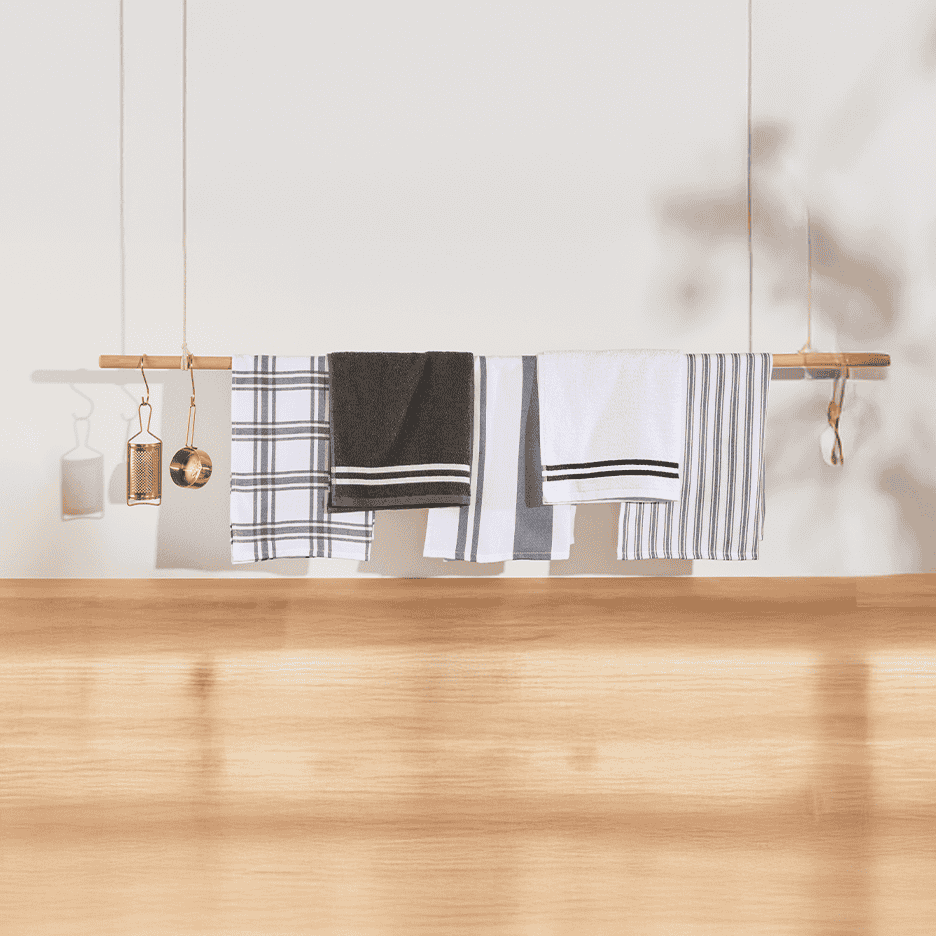 Et udvalg af køkkenhåndklæder i sort, hvid og grå med forskellige mønstre hængende på en træstang.