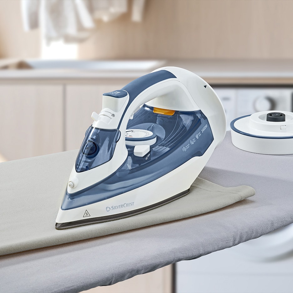 Dampstrygejern på et strygebræt med en vaskemaskine i baggrunden.