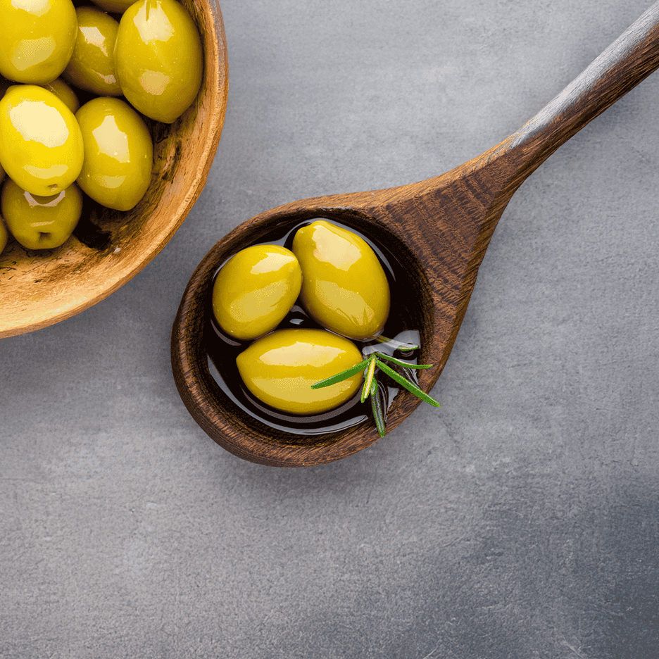 Grønne oliven i en træskål og en træske med olivenolie og rosmarin.