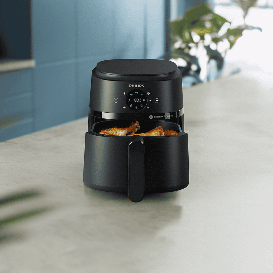 Sort airfryer med kyllingelår i kurven, placeret på en køkkenbordplade.