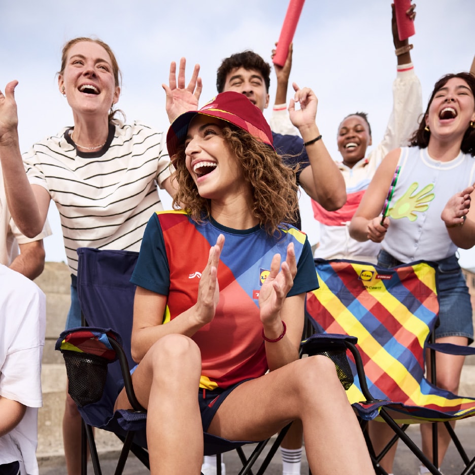 Glade fans i farverigt sportstøj og en foldestol med ternet mønster.