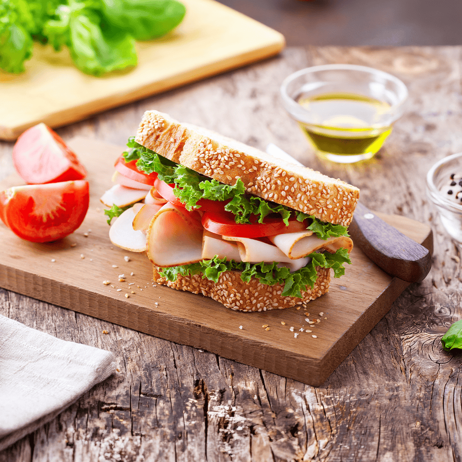 Sandwich med kalkunpålæg, salat og tomat på et træskærebræt.