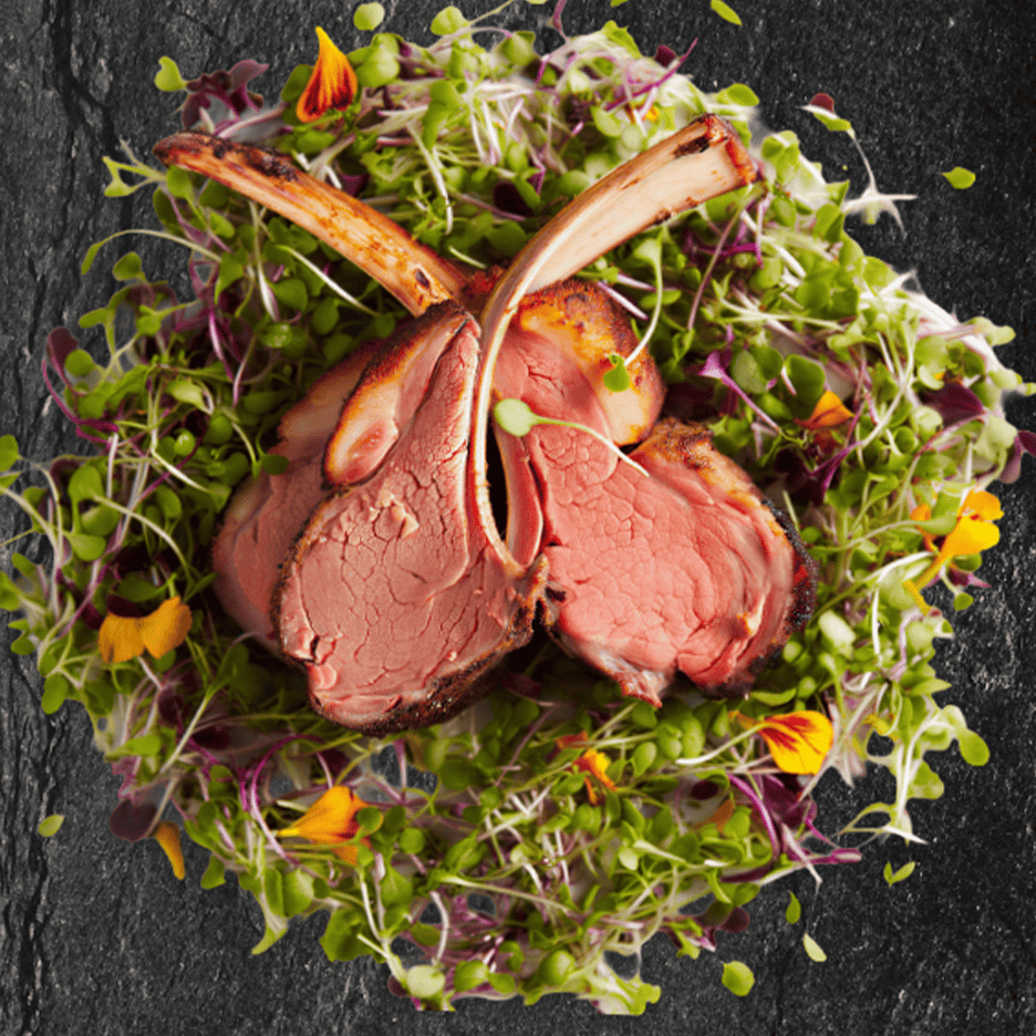 Lammekoteletter serveret på en seng af friske spirer og spiselige blomster.