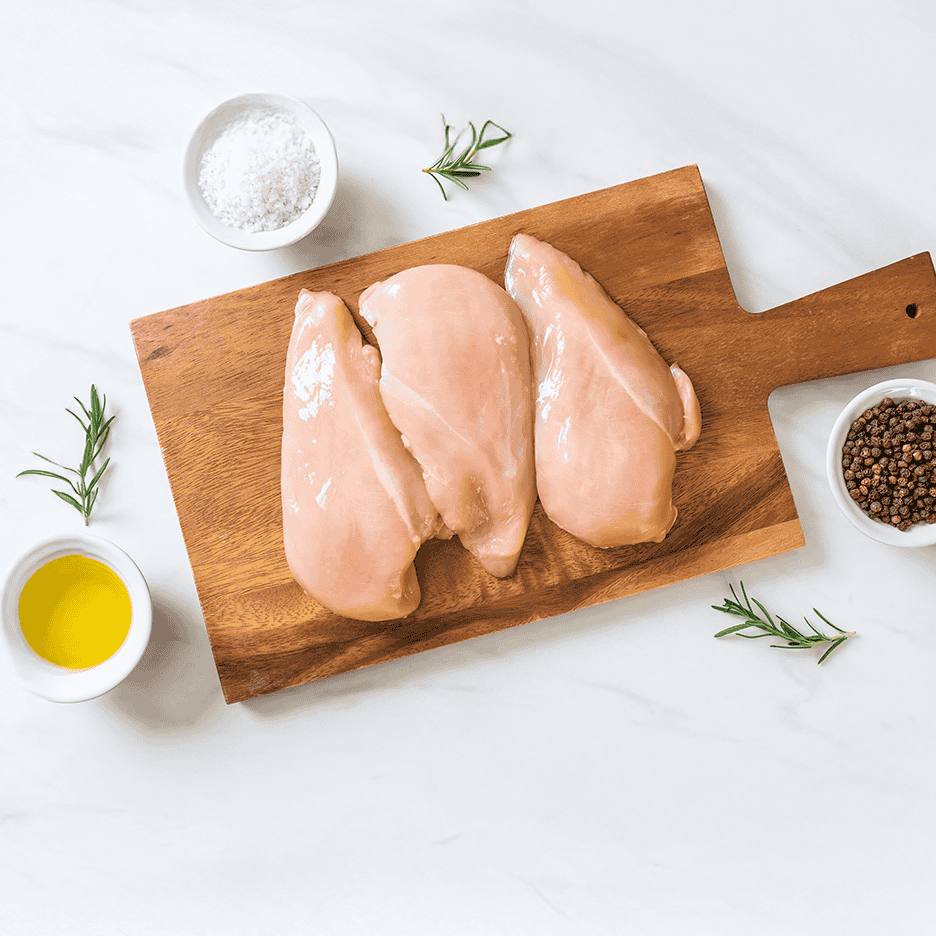 Rå kyllingebrystfileter på et skærebræt med rosmarin, salt, peberkorn og olivenolie.