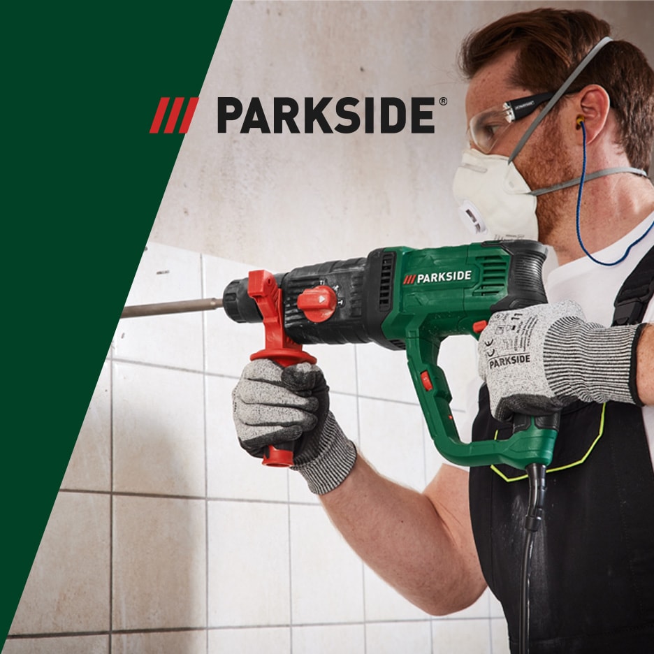 Mand med sikkerhedsudstyr bruger en borehammer til at bore i en væg.