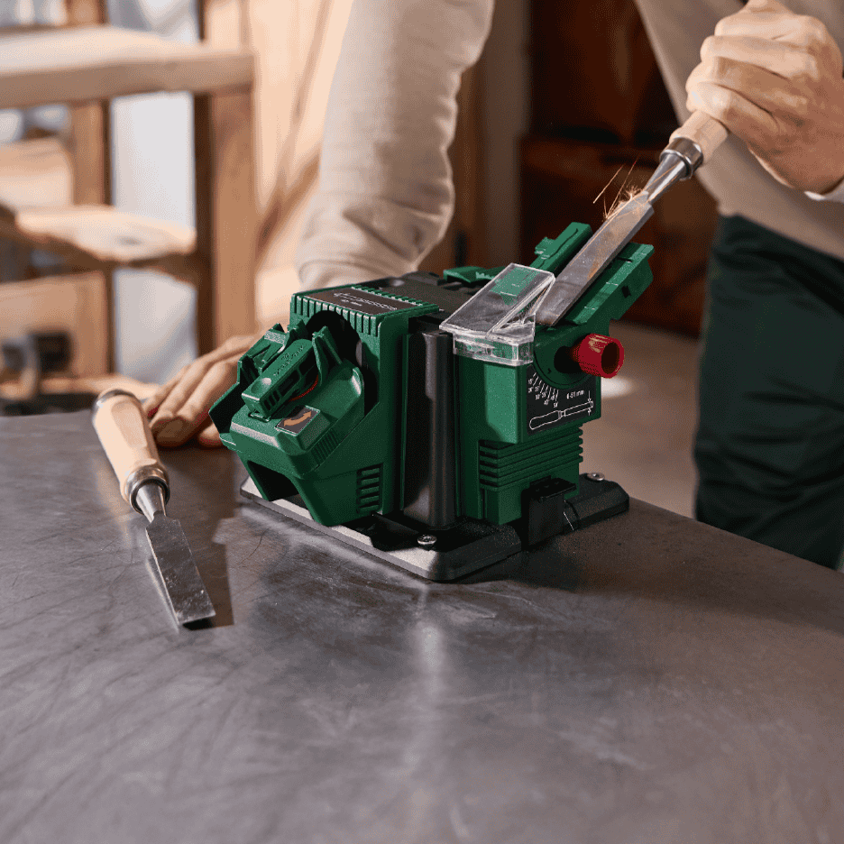 En person sliber et stemmejern med en grøn slibemaskine på et værkstedsbord.