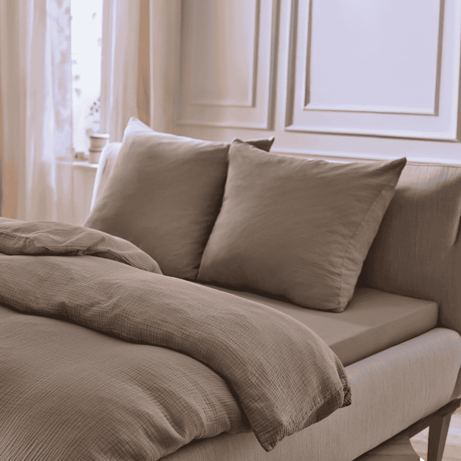 Sengelinned i brunt musselin med matchende puder og lagen i et lyst soveværelse.