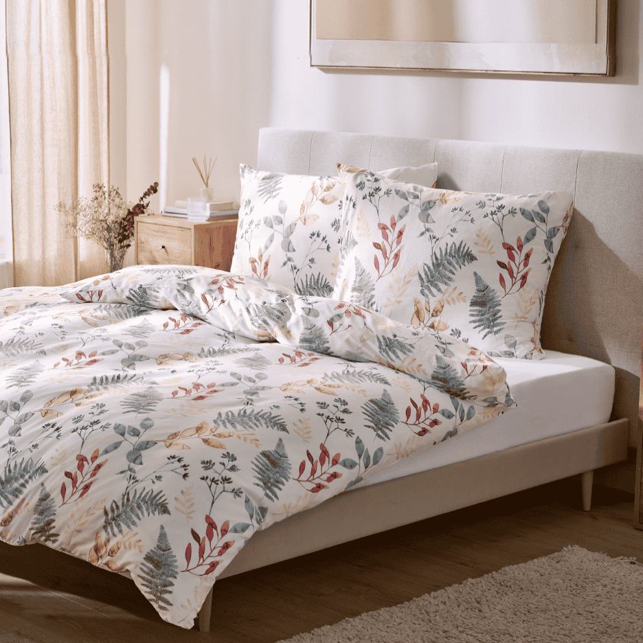 Sengesæt med botanisk mønster i et lyst soveværelse med træmøbler.