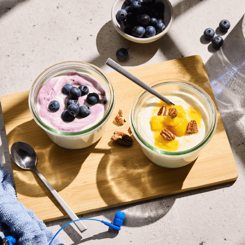 To glas yoghurt med frugt og nødder på et træskærebræt, med blåbær og høretelefoner.