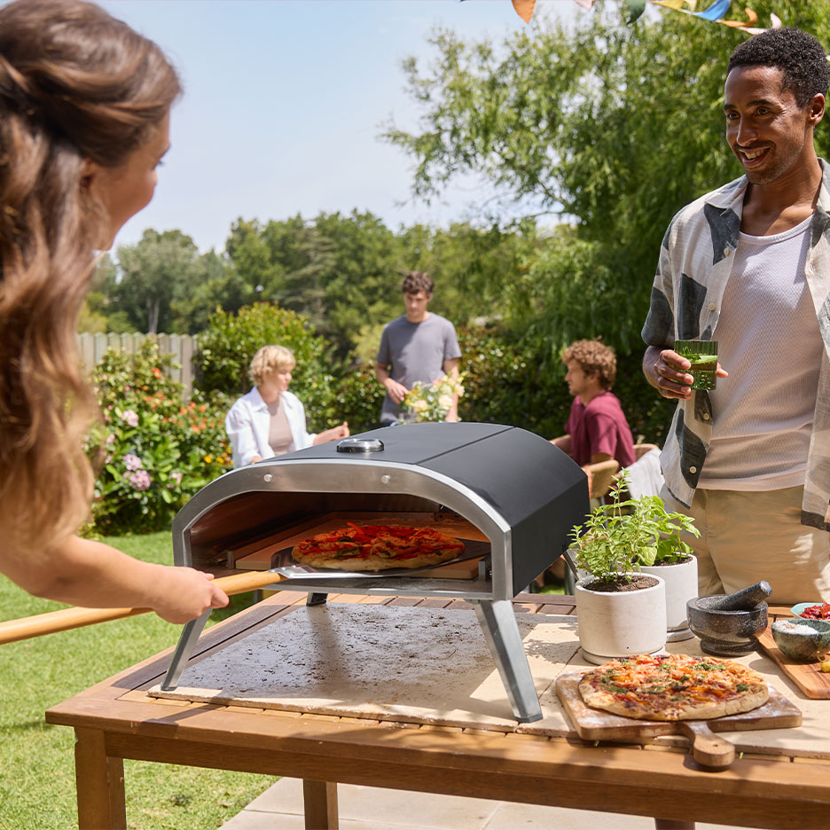 Familie til havefest, kvinde lægger pizza i ovn, mand holder en drink.
